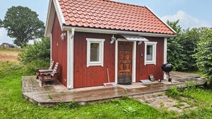 A small red wooden house with a tiled roof, a porch with a bench, and a barbecue grill. - 1 bedroom amazing home in Blomstermåla (Blomstermåla)