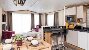 A modern kitchen with a microwave, a coffee machine, and a dining area with a table set for two. - Autograph Junior Lodge 2 Bed with Hot Tub (Ormside, Appleby-in-Westmorland)