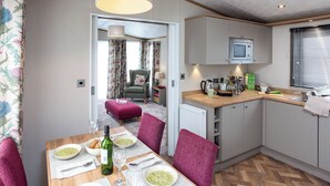 A compact kitchen with a dining area, a radiator, and a window with blinds. - Autograph Junior Lodge 2 Bed with Hot Tub (Ormside, Appleby-in-Westmorland)