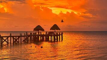A pier with thatched-roof structures, extending into calm waters at sunset.