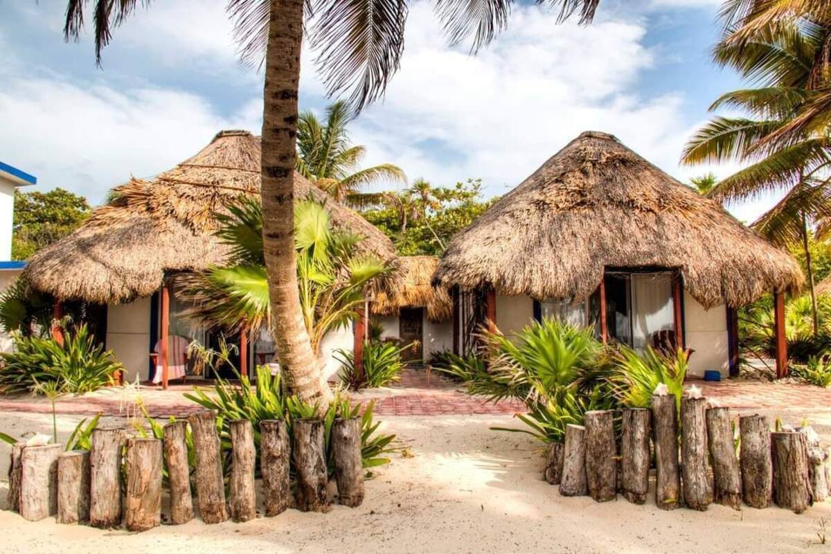 Un resort con cabañas de techo de paja, palmeras y un sendero arenoso.