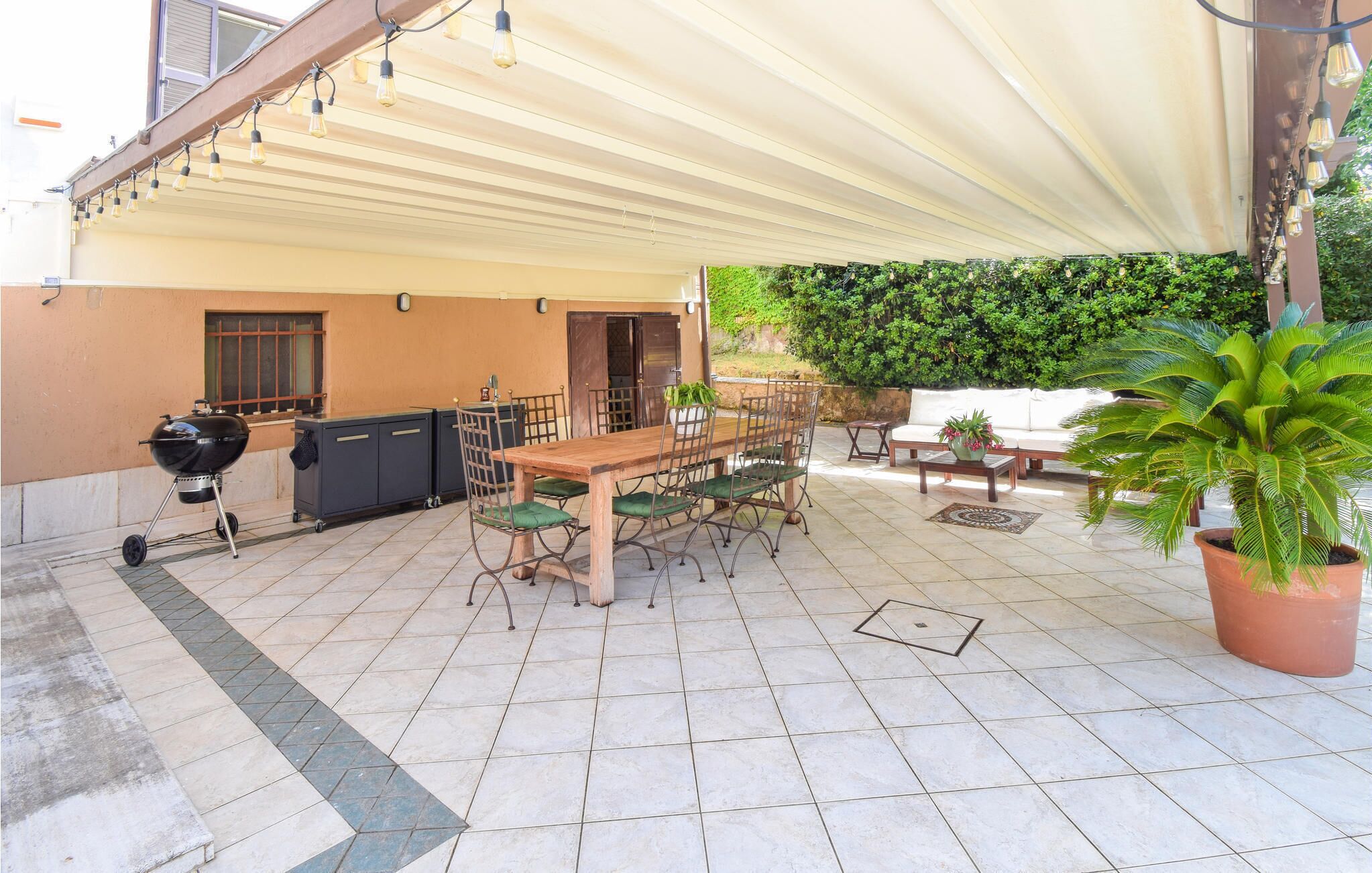 An outdoor patio with a wooden table and chairs, a barbecue grill, and a covered area with a white canopy.