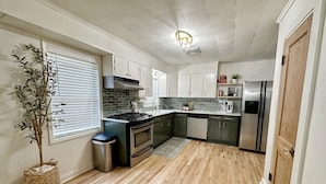 Cocina compacta con estufa a gas, horno, lavavajillas y refrigerador de acero inoxidable.