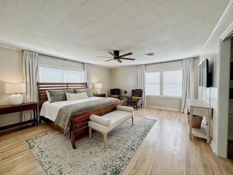 A bedroom with a bed, bedside tables, a chair, a desk, a television, and a ceiling fan.