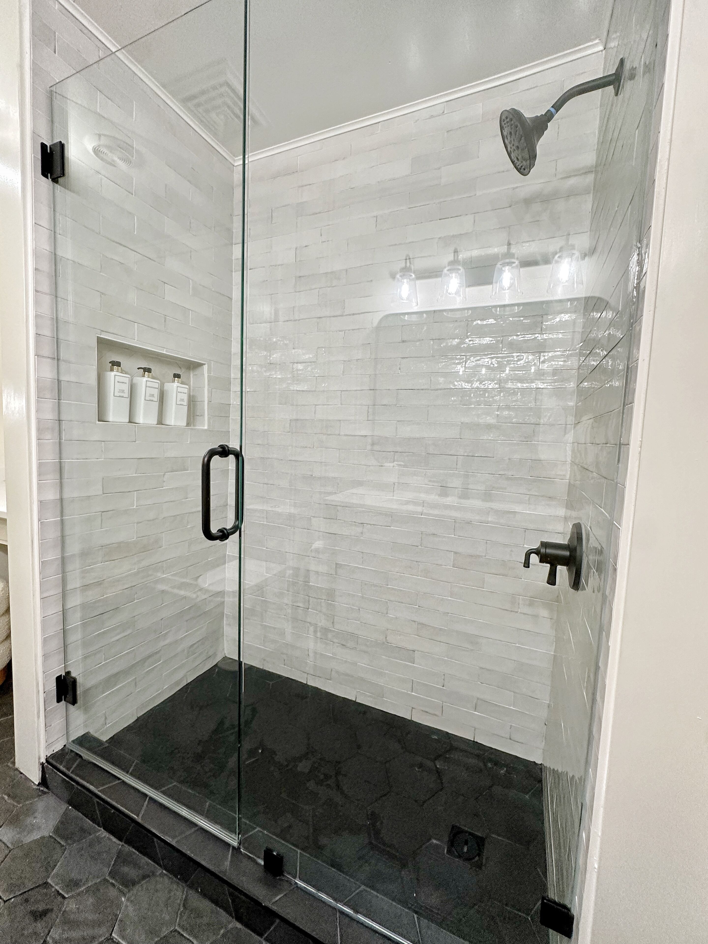 A glass-enclosed shower with a handheld showerhead and a wall-mounted faucet.