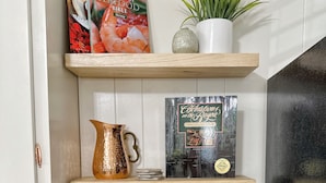 Una cocina con cafetera, libro de cocina y adornos en estantes.