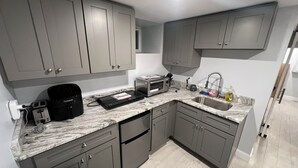 A modern kitchen with grey cabinets, a marble countertop, a built-in oven, and a sink. - Cozy basement/studio apartment with kitchenette and bathroom! (Boston)