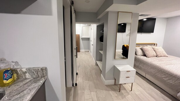 A modern bedroom with a bed, a dresser, a mirror, and a TV. - Cozy basement/studio apartment with kitchenette and bathroom! (Boston)
