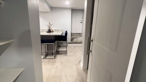 A narrow hallway with a staircase on the left, a dining area with a table and chairs in the center, and a door on the right. - Cozy basement/studio apartment with kitchenette and bathroom! (Boston)