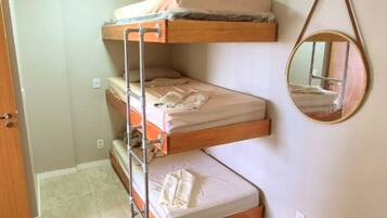 Una cama litera con escalera de metal, un espejo redondo en la pared y una puerta a la izquierda.