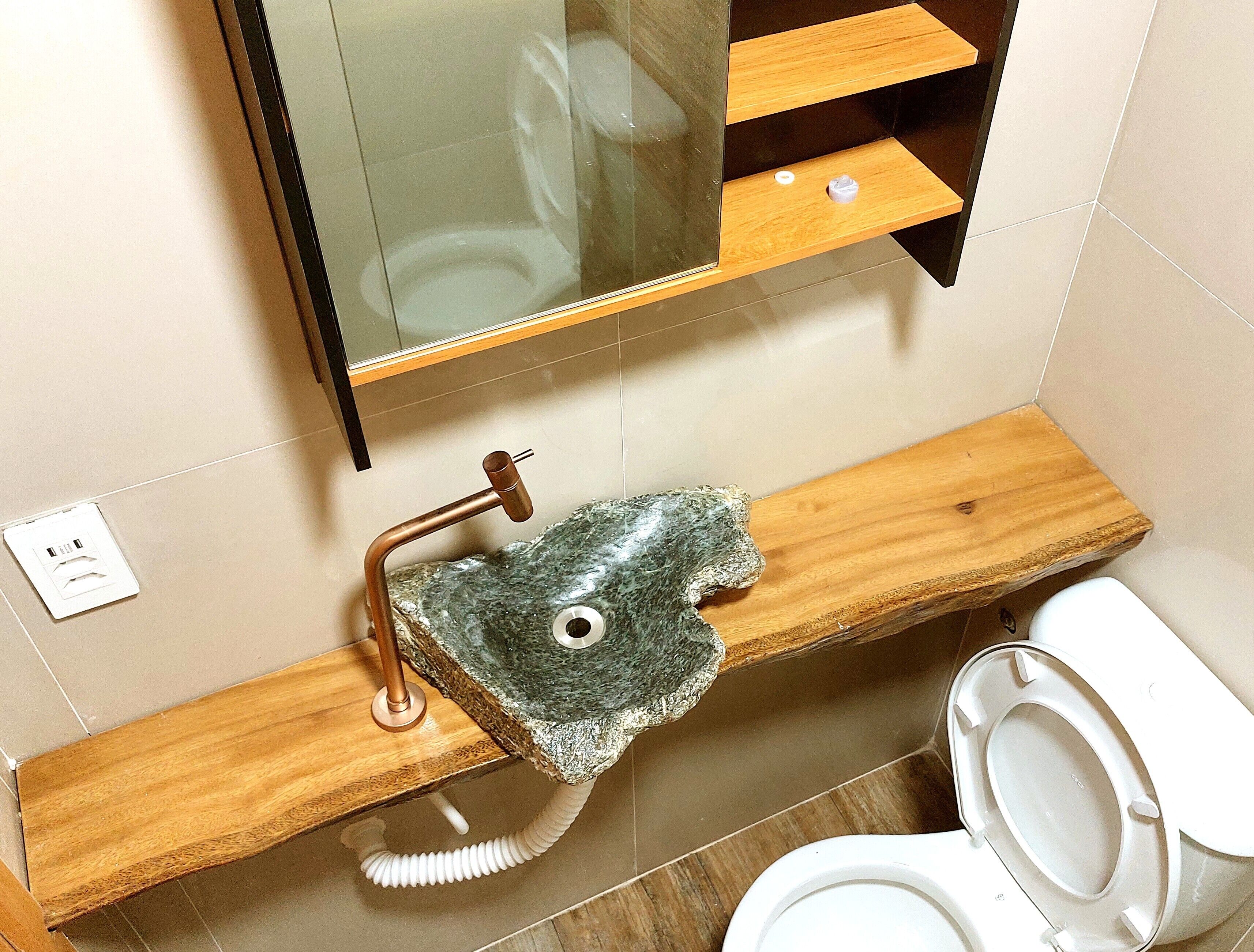 A bathroom with a wooden vanity, a sink with a stone-like faucet, and a toilet.