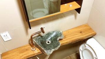A bathroom with a wooden vanity, a sink with a stone-like faucet, and a toilet.