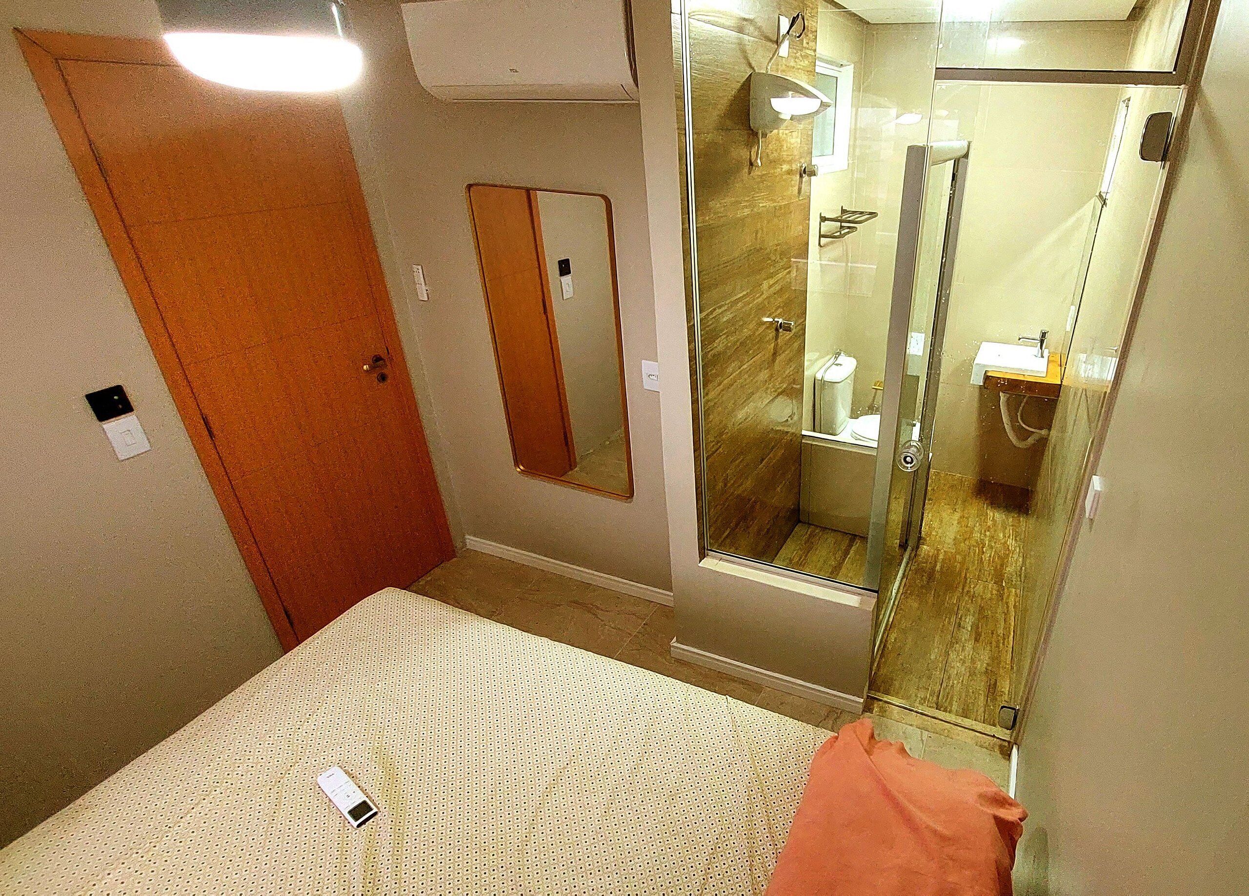 Una habitación de hotel con cama, baño con cabina de ducha de vidrio y espejo en la pared.