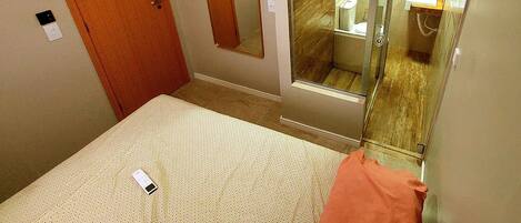 Una habitación de hotel con cama, baño con cabina de ducha de vidrio y espejo en la pared.