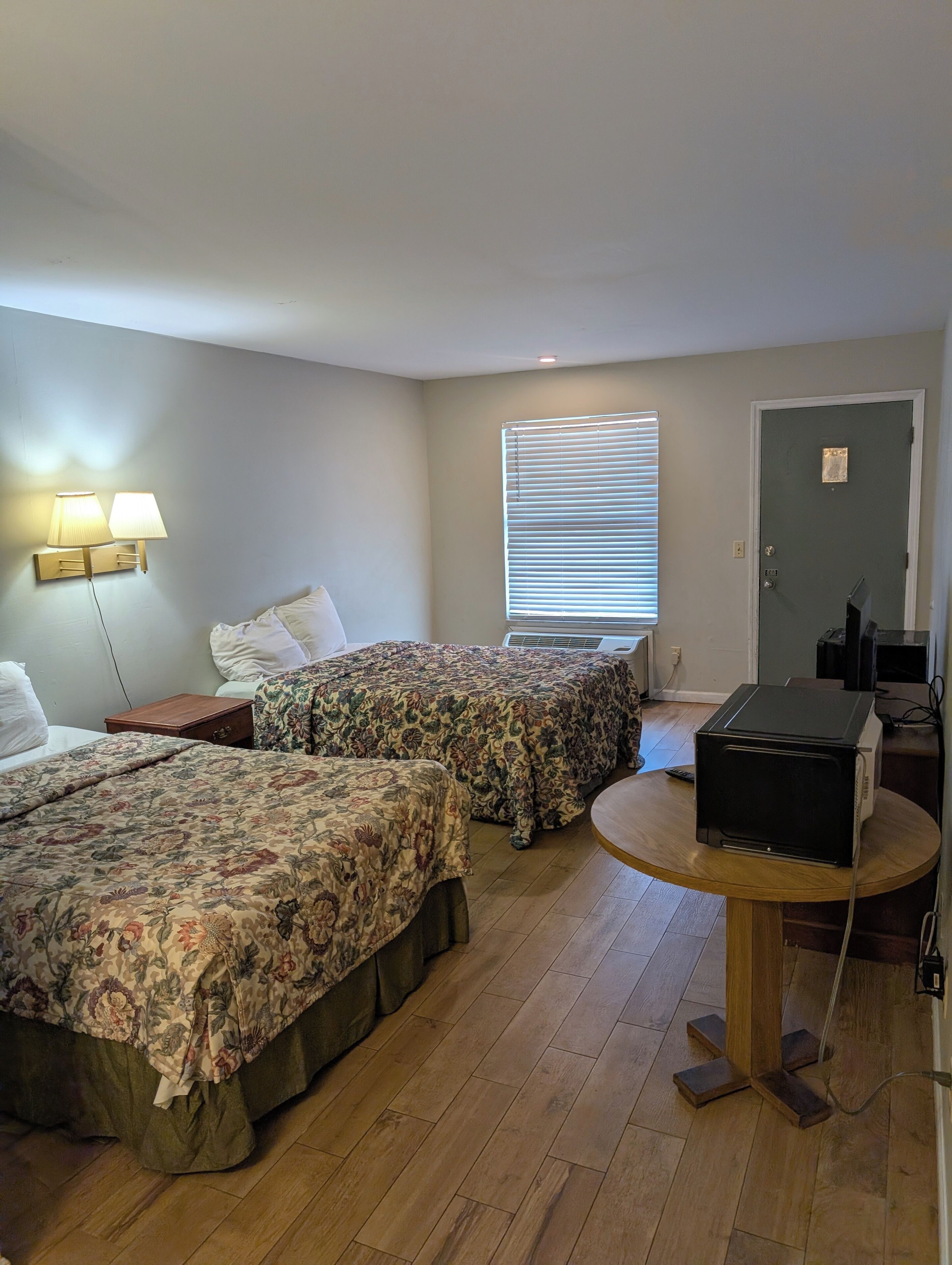 Une chambre d’hôtel avec deux lits, une petite table, un four à micro-ondes et une fenêtre avec des stores.
