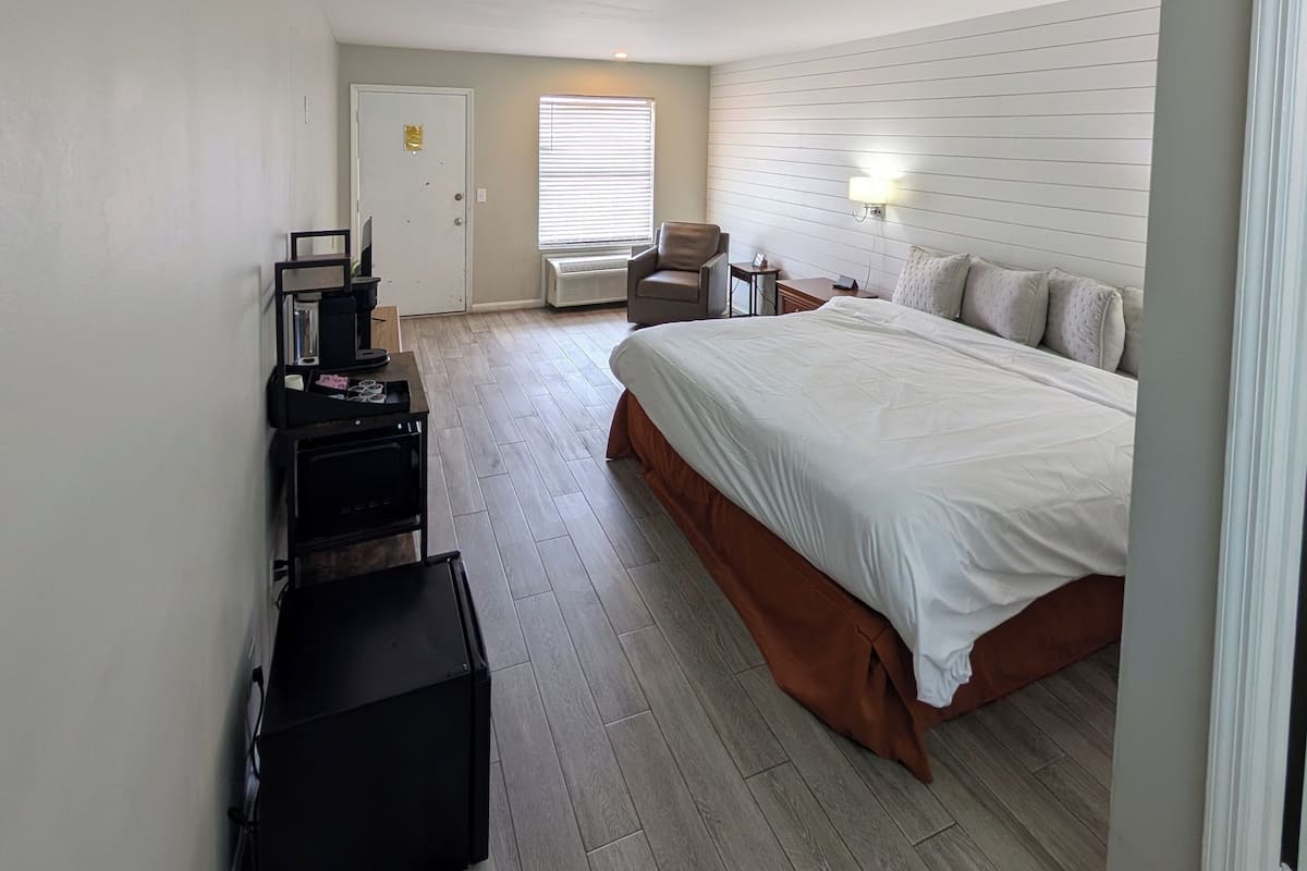 A hotel room with a large bed, a desk with a chair, a small table, and a suitcase.