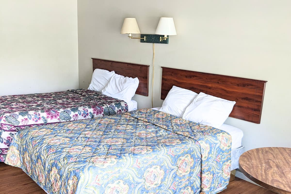 A hotel room with two beds, a wooden headboard, a small round table, and a chair.