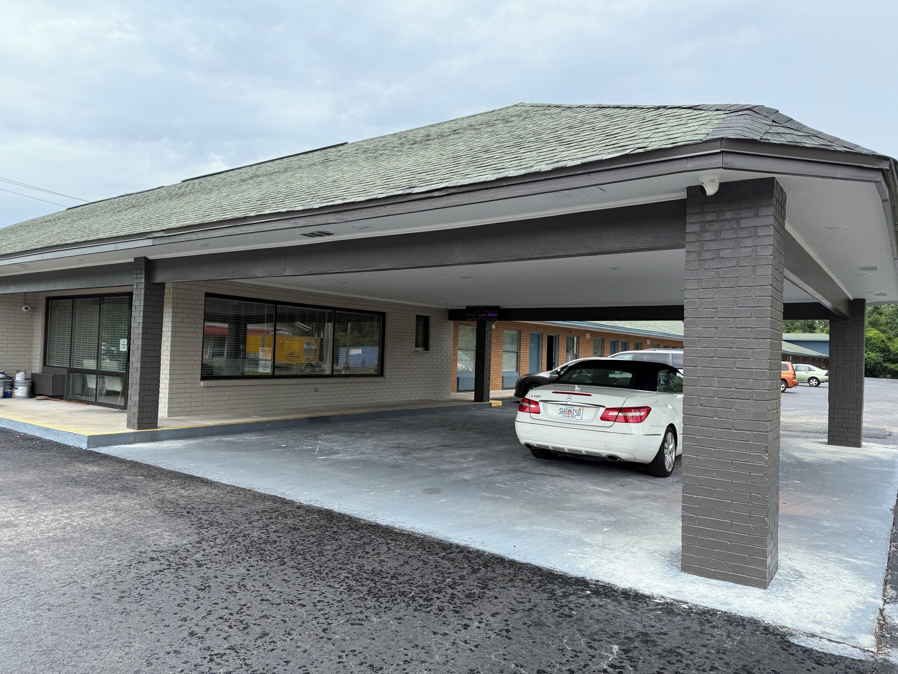 A building with a covered parking area, a white car parked inside, and a brick pillar.