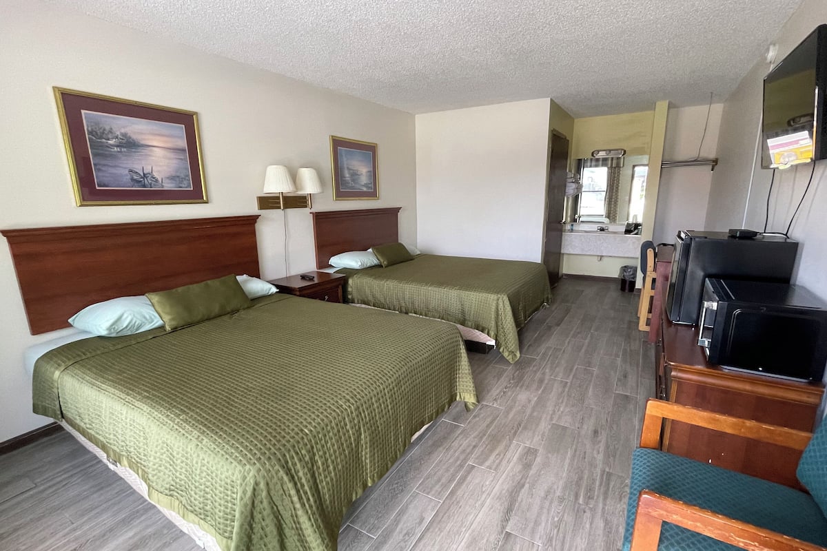 A hotel room with two beds, a desk with a chair, a television, and a bathroom visible through an open door.