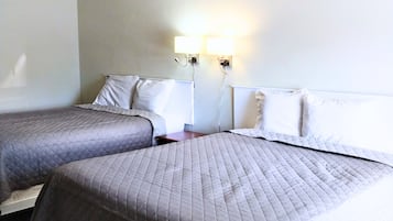 A hotel room with two beds, each with a grey quilted bedspread and white pillows. There are wall-mounted nightstands with lamps between the beds.