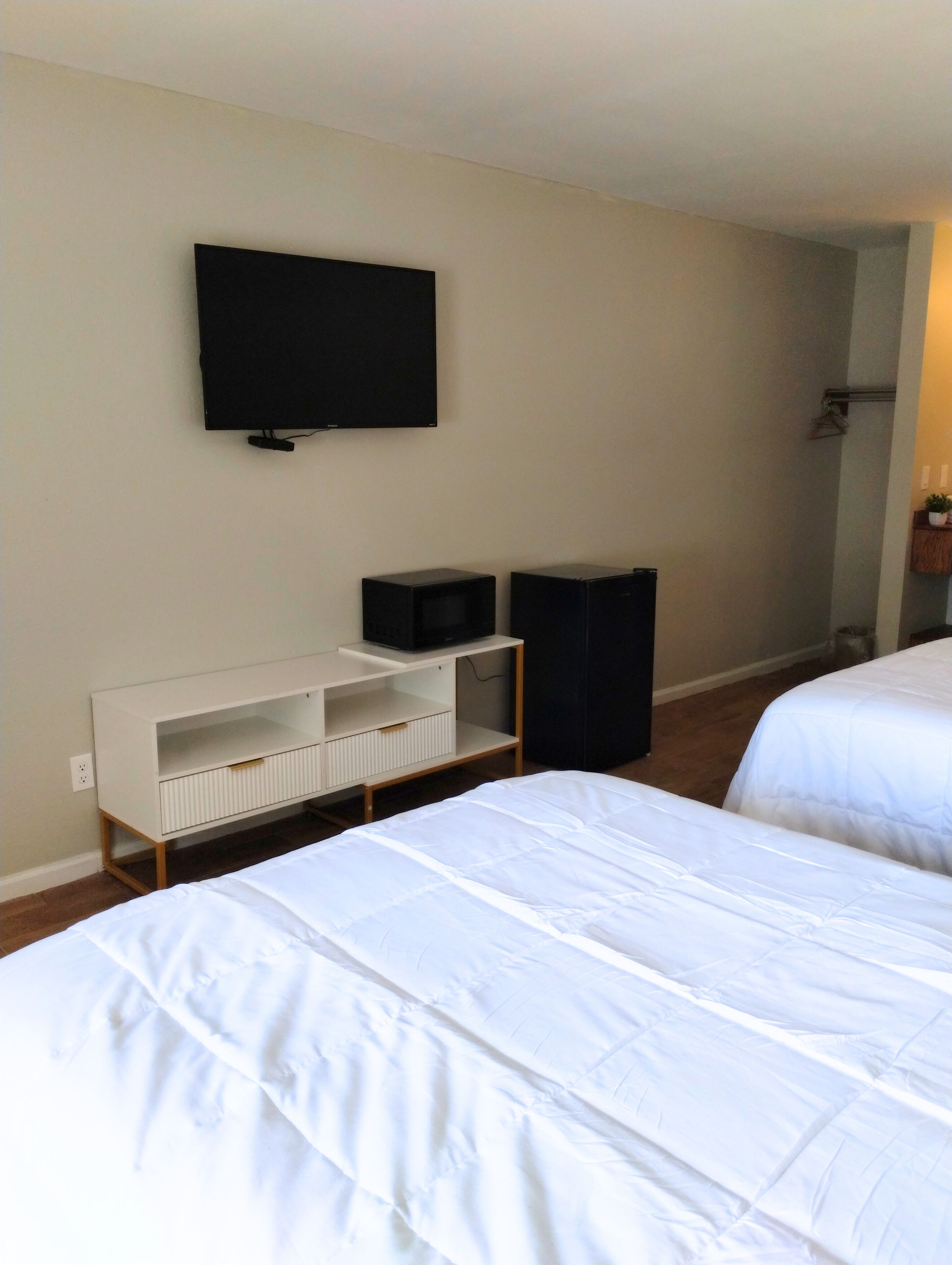 Une chambre d’hôtel avec deux lits, un téléviseur fixé au mur, une petite armoire blanche et une poubelle noire.