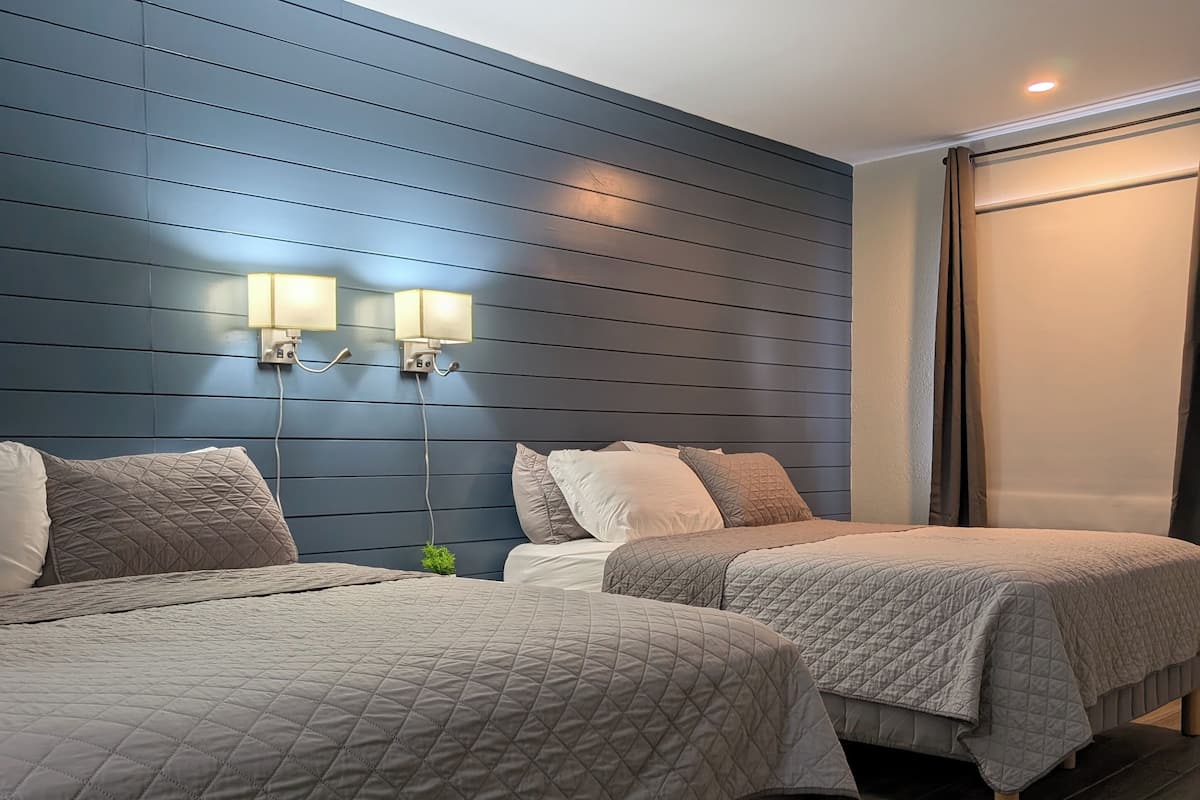 A hotel room with two beds, a blue wall, and a window with curtains.