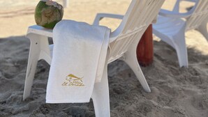 Una silla de playa con una toalla y un coco, todo bajo un toldo de paja.