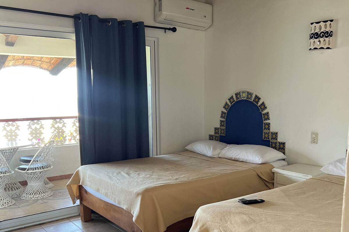 A bedroom with two beds, a ceiling fan, an air conditioning unit, and a balcony with outdoor furniture.