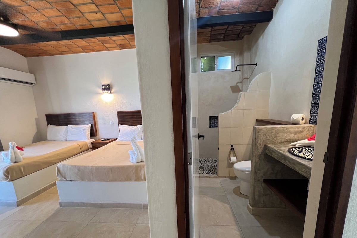 A hotel room with two beds, a shower, and a bathroom with a sink and toilet.