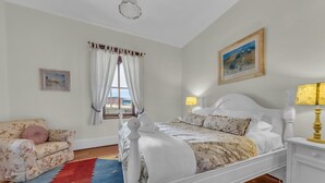 A bedroom with a white bed, a floral sofa, a red and blue rug, and a painting on the wall. - Munns Tower House- In the Heart of Merimbula (Merimbula)
