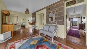 A spacious living area with a large rug, a white sofa, and a stone wall. - Munns Tower House- In the Heart of Merimbula (Merimbula)