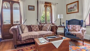 A living room with a brown leather sofa, a blue armchair, a wooden coffee table, and a colorful rug. - Munns Tower House- In the Heart of Merimbula (Merimbula)