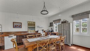 A spacious kitchen with a wooden dining table, wicker chairs, and a hanging chandelier. - Munns Tower House- In the Heart of Merimbula (Merimbula)