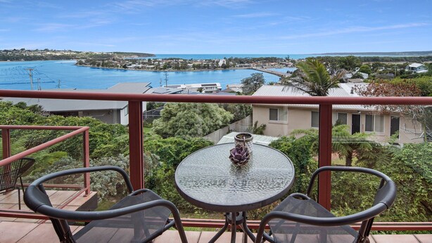 A balcony with a table and chairs overlooking a coastal area with a pool and buildings. - Pacific Heights - Standard Apartment (Merimbula)
