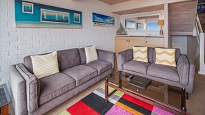 A living room with two grey sofas, a glass coffee table, and a colorful striped rug. - Pacific Heights - Standard Apartment (Merimbula)