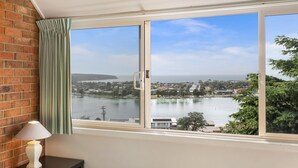 A bedroom with a large window overlooking a lake and a residential area. - Pacific Heights - Standard Apartment (Merimbula)