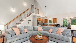 Ein geräumiges Wohnzimmer mit einem grauen Ecksofa, einem Holztisch und einer Treppe, die zu einer oberen Ebene führt.