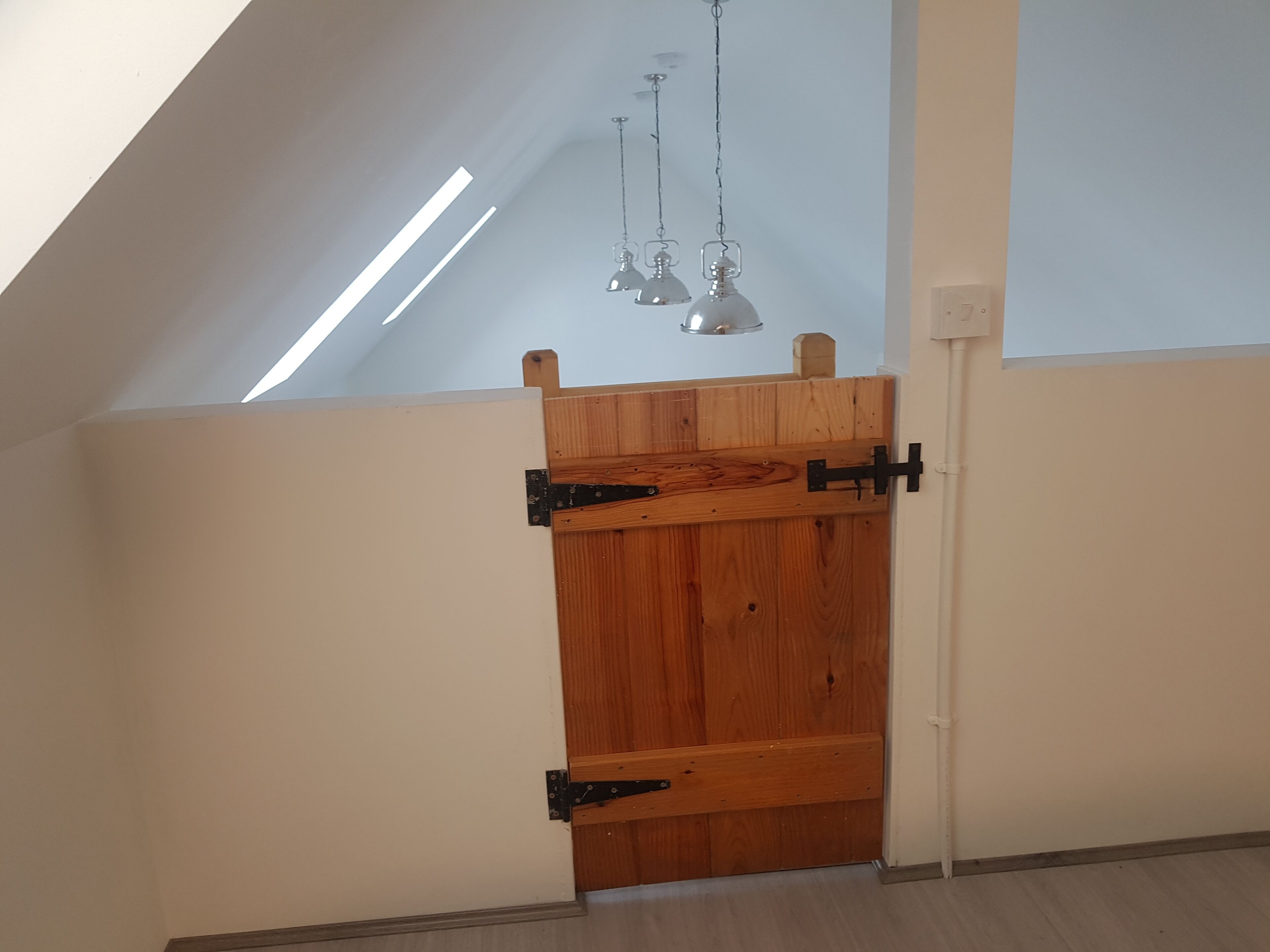 Una puerta de madera con bisagras negras en una habitación con techo inclinado y tragaluz.