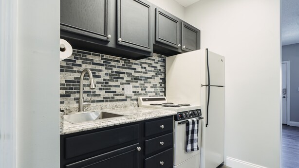 A compact kitchen with dark cabinets, a white refrigerator, a stove, and a tiled backsplash. - EXCELLENT location!!  Walk to The Island. (Pigeon Forge)