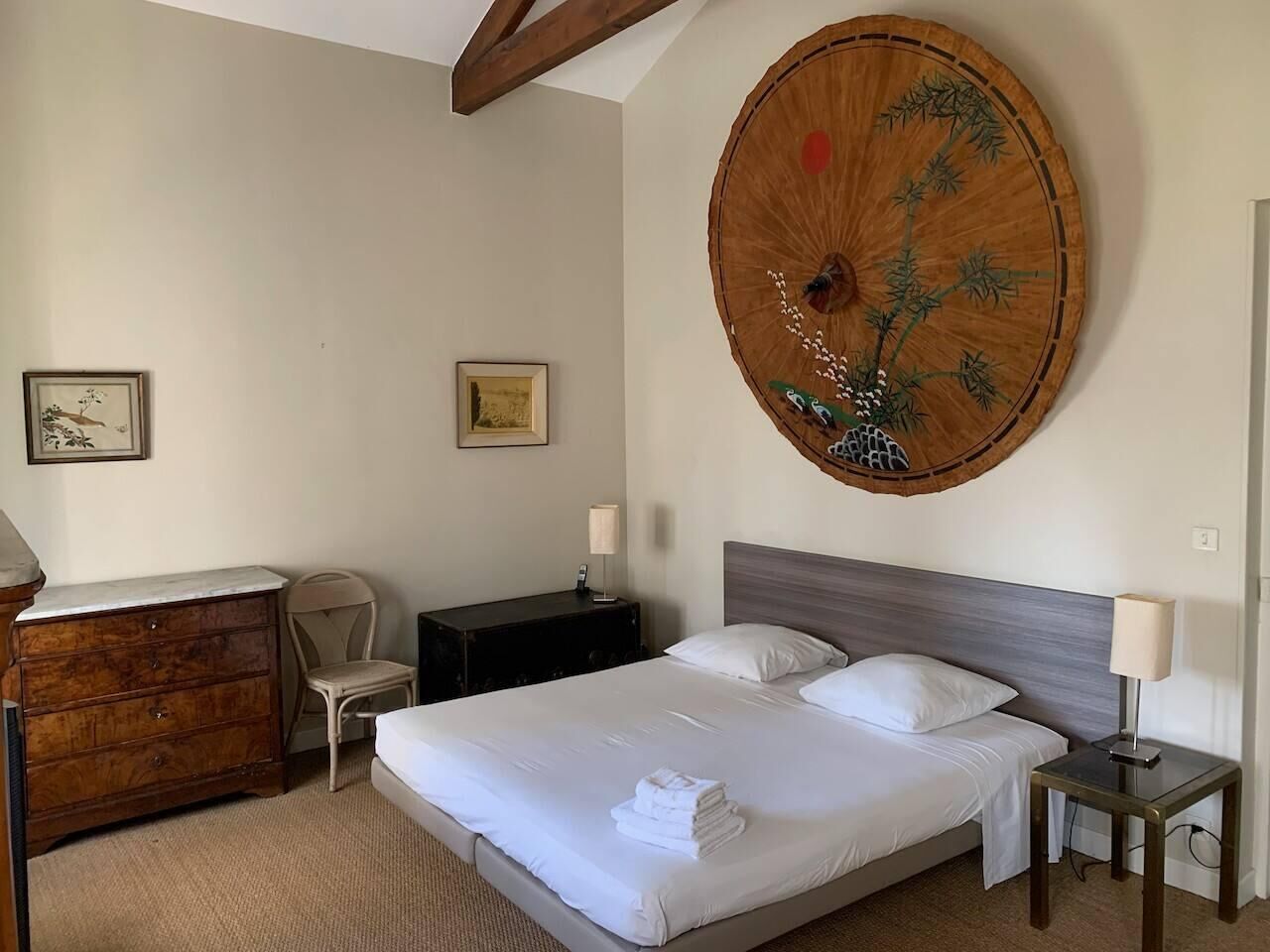 A hotel room with a bed, bedside tables, a dresser, and two framed pictures on the wall.