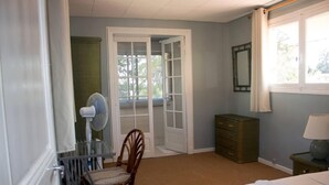 A bedroom with a bed, a chair, a dresser, a fan, and a window.