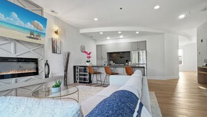 A modern living room with a fireplace, seating area, and a kitchen in the background. - Luxury 2Bed w/ Amazing Views (Cornelius)