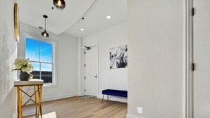 A spacious room with wooden flooring, a large window, a blue bench, and a wall-mounted abstract painting. - Luxury 2Bed w/ Amazing Views (Cornelius)