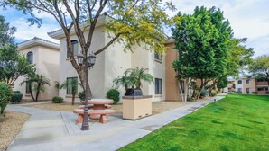 A residential area with a paved walkway, a round table with chairs, and a large tree. - KING Beds, Heated Community Pool! 3 miles from Cardinal Stadium! (Phoenix)
