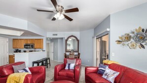 A modern living room with red leather sofas, a ceiling fan, and a kitchen in the background. - KING Beds, Heated Community Pool! 3 miles from Cardinal Stadium! (Phoenix)