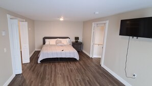 A bedroom with a bed, a nightstand, a TV, and a door. - Coastal Charm by the Bay: 4 Bedroom Apartment next to Yarmouth CAT Ferry (Yarmouth)