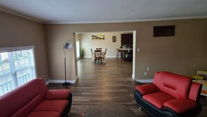 A spacious living room with a wooden floor, two red sofas, a floor lamp, and a dining area in the background. - Coastal Charm by the Bay: 4 Bedroom Apartment next to Yarmouth CAT Ferry (Yarmouth)