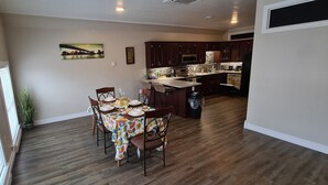A dining area with a table set for four, a kitchen in the background, and a cityscape painting on the wall. - Coastal Charm by the Bay: 4 Bedroom Apartment next to Yarmouth CAT Ferry (Yarmouth)