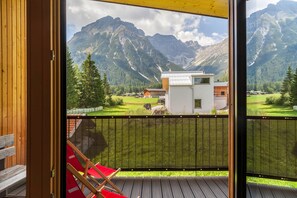 Un balcon avec vue sur les montagnes, une terrasse en bois et une chaise rouge.