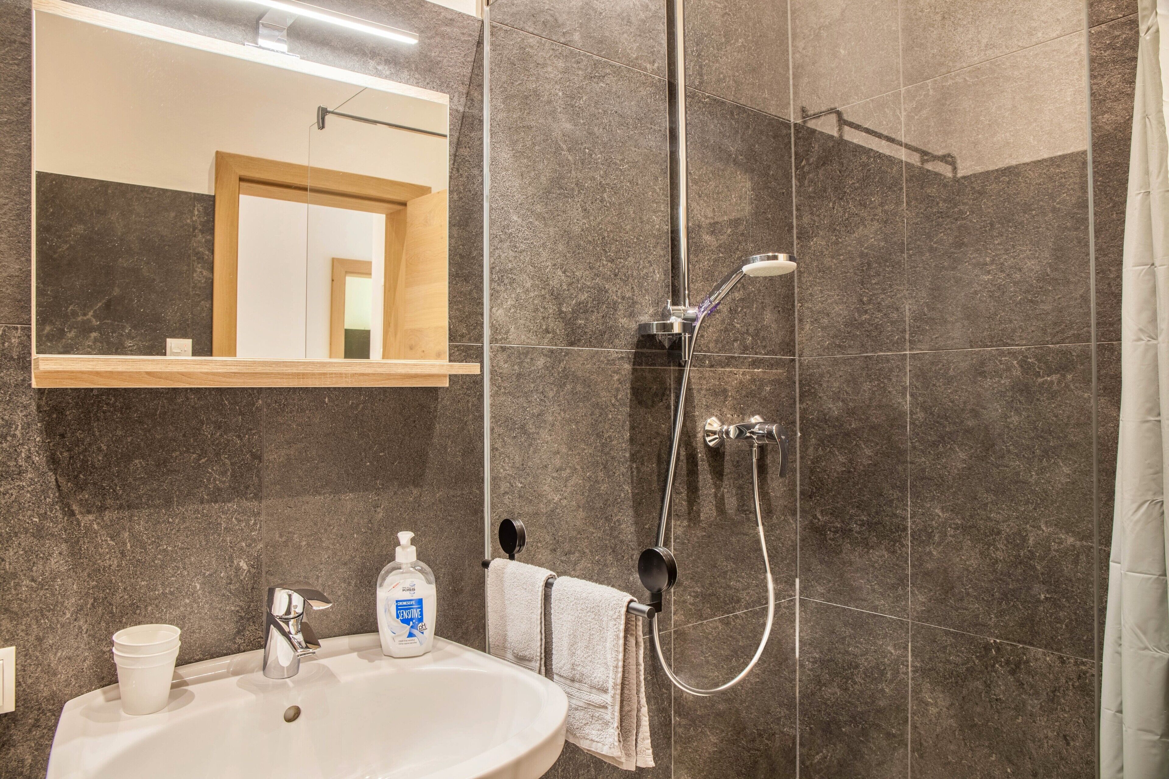 Un baño con lavamanos, espejo, ducha y toallero.